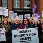 A group of women holding banners and placards at a WASPI rally outside a government building, advocating for state pension age compensation.
