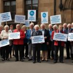 A group of pensioners holding banners outside a Scottish government building, celebrating the reinstatement of the universal Pension Age Winter Heating Payment in 2025.