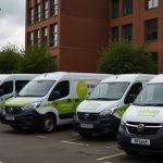 A line of electric vans parked outside a DVLA office, showcasing new driving licence rules for zero-emission vehicles in June 2025.