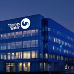 A modern office building with the Thames Water logo illuminated against a twilight sky, reflecting the company’s ongoing financial challenges.
