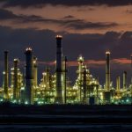 A large oil refinery with tall chimneys and illuminated structures against a twilight sky, reflecting BP's industrial operations.