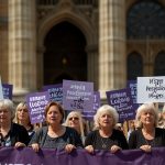 A large group of women holding banners and signs at a WASPI campaign rally in London, advocating for compensation due to State Pension age changes, with a backdrop of Parliament.