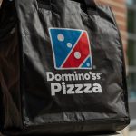 Domino’s Pizza logo with a DoorDash delivery bag, symbolizing their expanded partnership announced on September 16, 2025, driving a stock price surge.