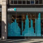 Next plc logo on a London storefront with rising stock chart overlay showing 3% gain on FTSE 100, October 29 2025