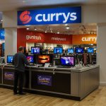 A bustling Currys electronics store with vibrant displays of laptops and TVs, reflecting the retailer’s strong sales and share buyback announcement boosting investor confidence.