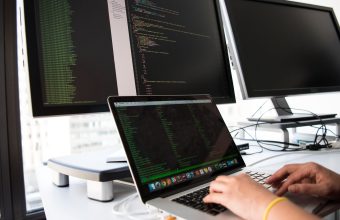 Developer writing code for a custom web application across multiple monitors