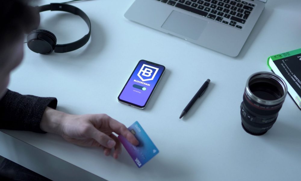 Person holding a crypto payment card beside a smartphone showing a blockchain app