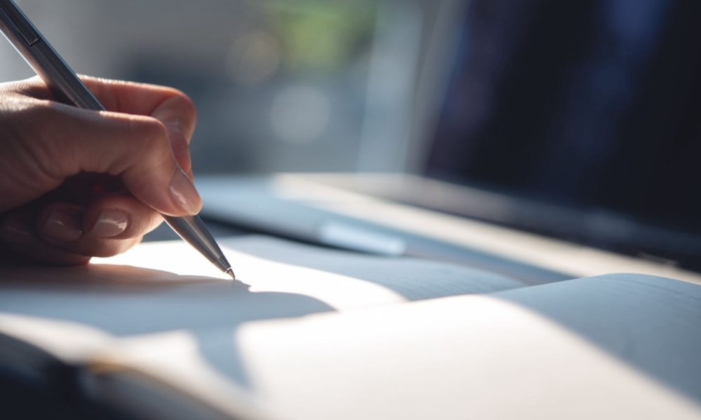 A hand writing with a pen in an open notebook, echoing the handwritten letters at the heart of Diverse Referrals' homeowner outreach
