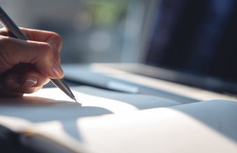 A hand writing with a pen in an open notebook, echoing the handwritten letters at the heart of Diverse Referrals' homeowner outreach