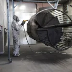 Operator spray finishing a metal part inside an industrial booth